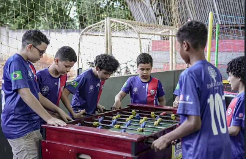 Grupo de 5 crianças brincando no pebolim no projeto instituto avivar